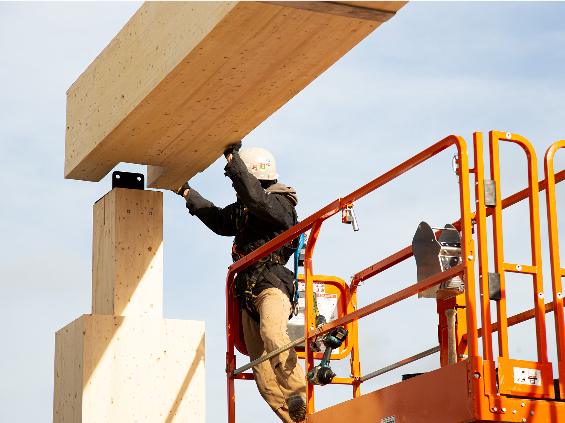 A worker attaching a mass timber cross beam on a construction site. 